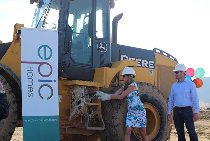 Epic Homes’ founder and president Christina Presley christens excavator with bottle of beer.  Watching is Epic Homes’ partner Bill Wood.